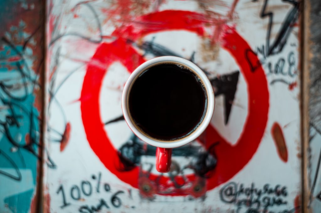 Picture of a black coffee sitting on top of a sign which has graffiti on it. The espresso cup contains a Padre coffee pods brew