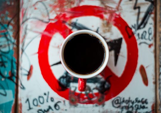 Picture of a black coffee sitting on top of a sign which has graffiti on it. The espresso cup contains a Padre coffee pods brew