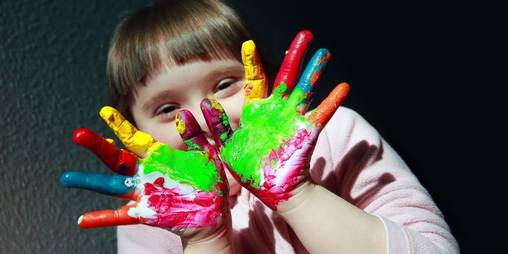 Picture of a young girls with colourful paint on her hand, as a child represented in Australia's Disability Strategy