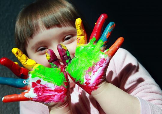 Picture of a young girls with colourful paint on her hand, as a child represented in Australia's Disability Strategy