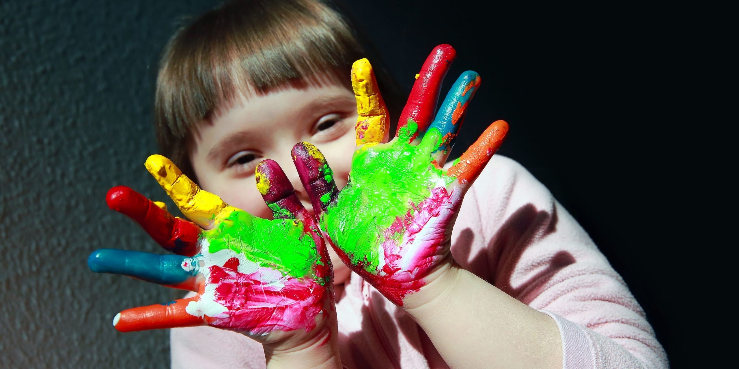 Picture of a young girls with colourful paint on her hand, as a child represented in Australia's Disability Strategy