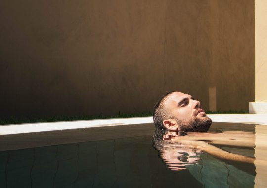 Man relaxing in a bath, with the water still and soft lighting. He is enjoying a spa package for men