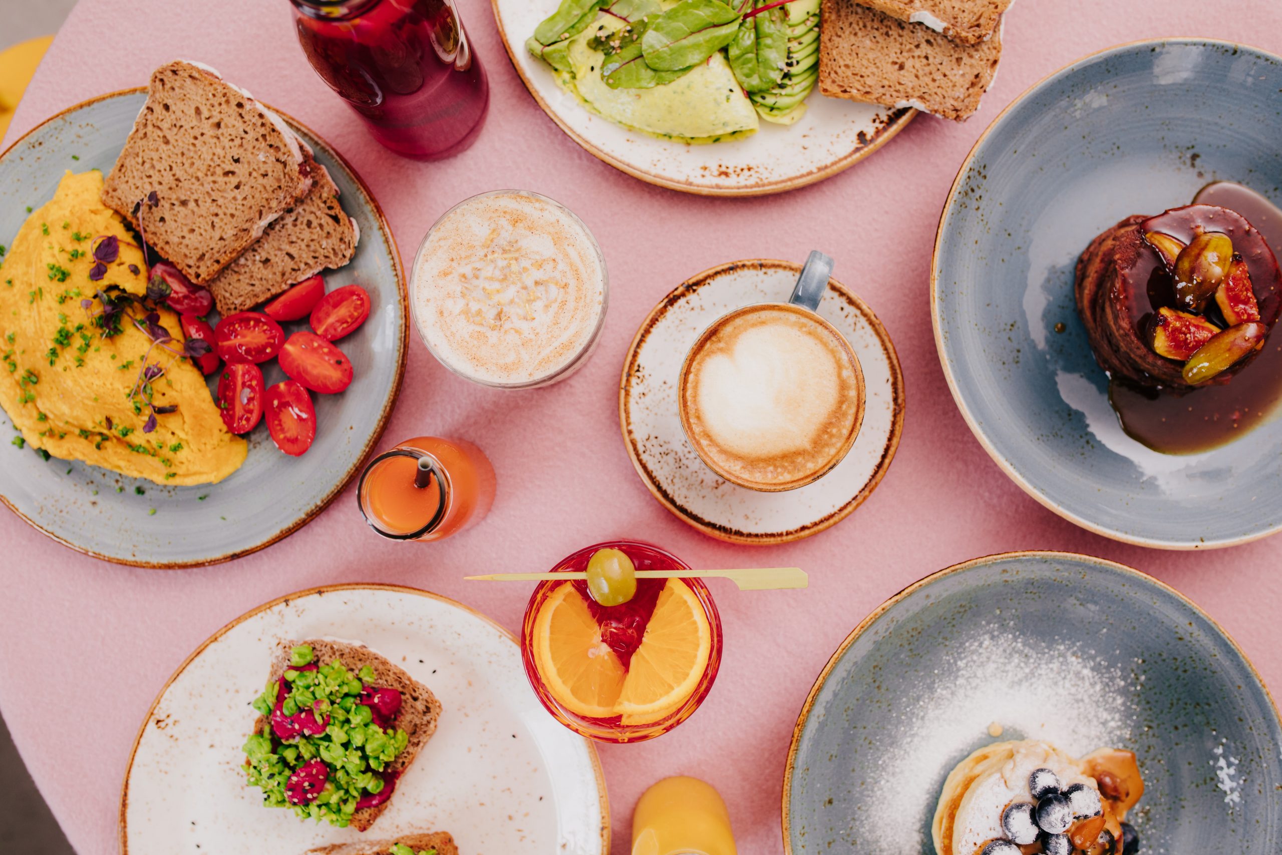 Flat-lay image of a food-laden table of bottomless brunch in Melbourne, including toast, pancakes, coffee, cocktail and juice