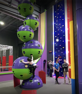 Picture of a large climbing wall made up of green and purple plastic bulbs, with a child climbing up the side