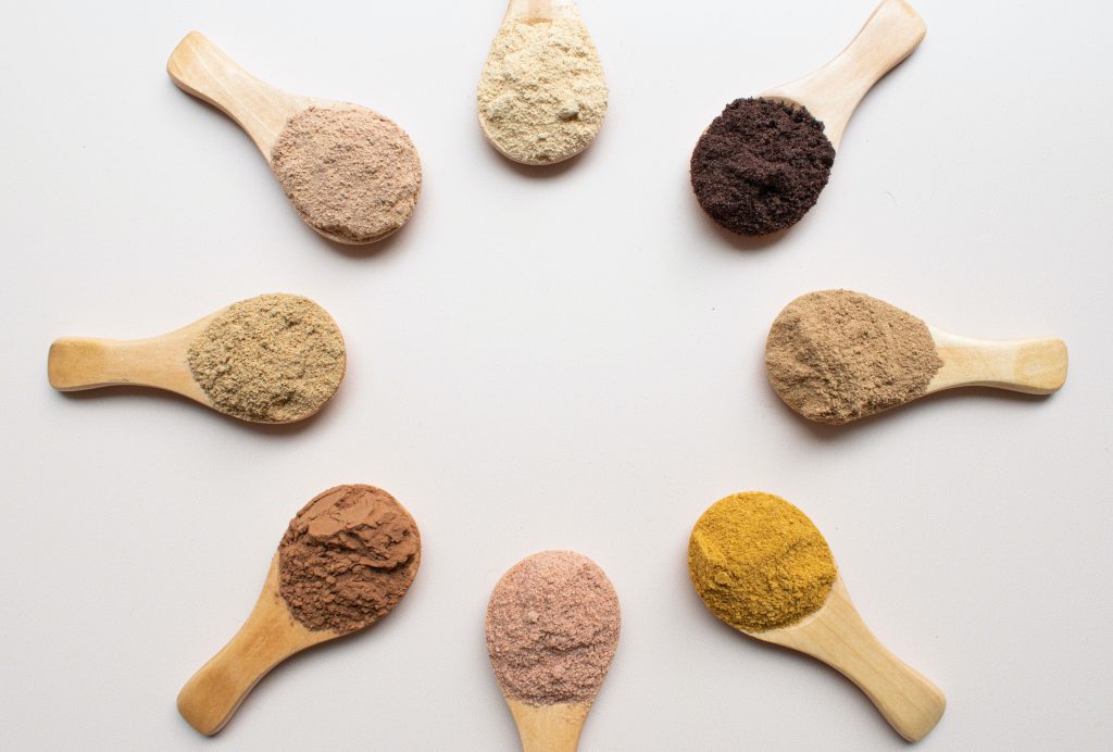 Picture of 8 spoons in a circle, each containing different protein powders and Nutra Organics collagen powder