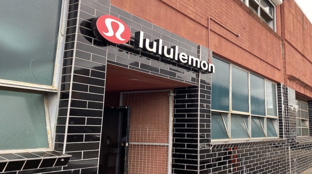 Picture of the lululemon logo on a black tiled wall, which is the entrance to the lululemon outlet in Melbourne