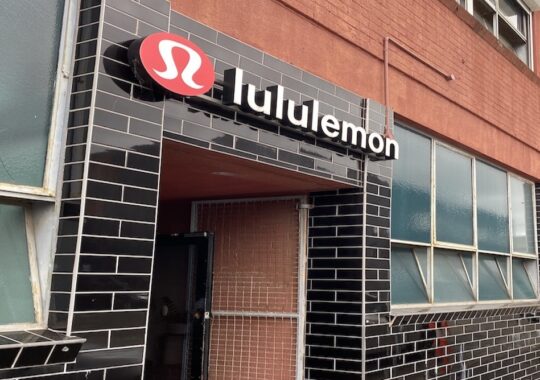 Picture of the lululemon logo on a black tiled wall, which is the entrance to the lululemon outlet in Melbourne