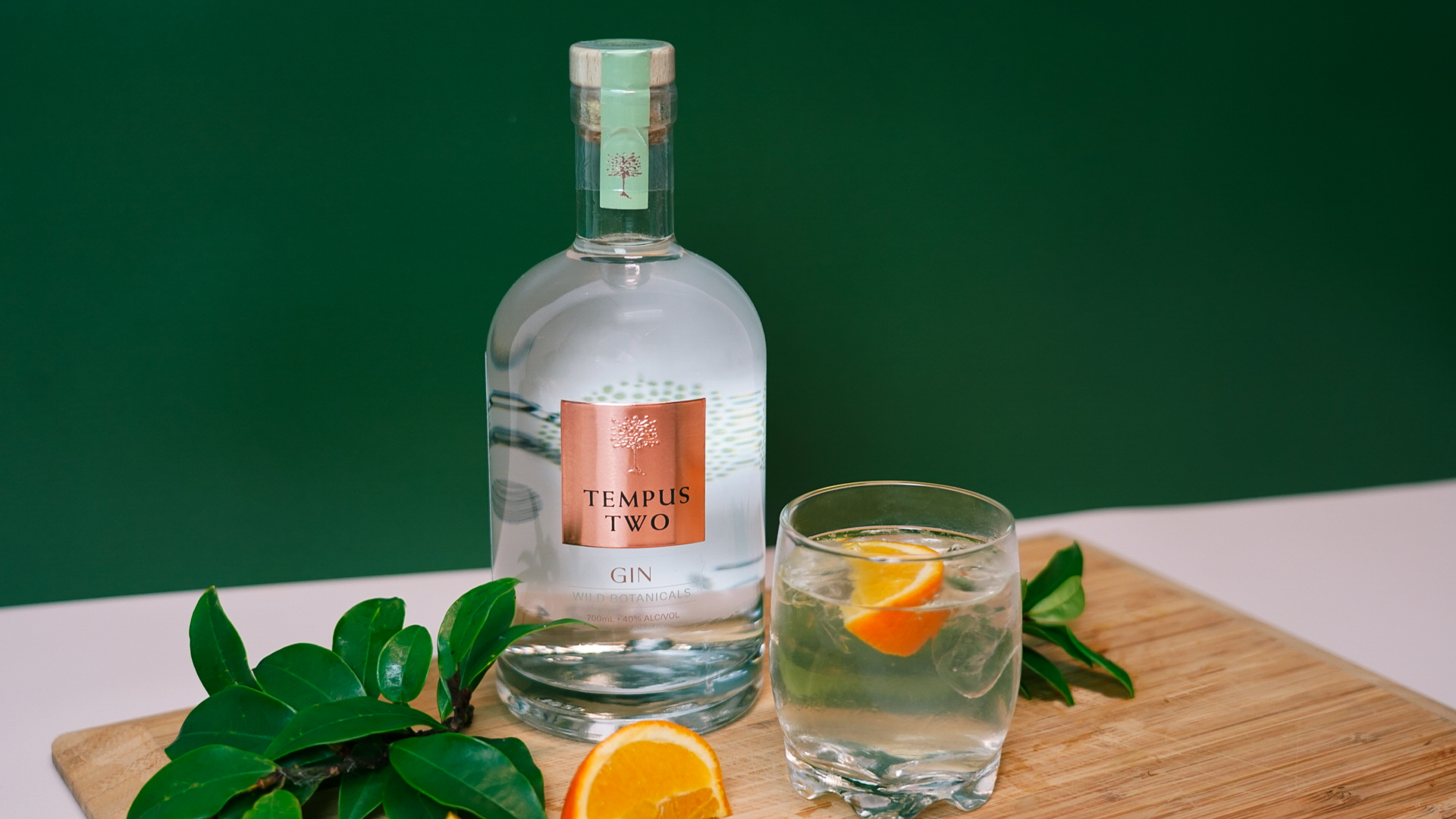 Picture of a Tempus Two gin bottle, with a glass of gin and organe slice in the glass and green garnish