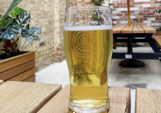 Picture of a pint of CoConspirators Brewing Company beer on a table in an outdoor beer garden