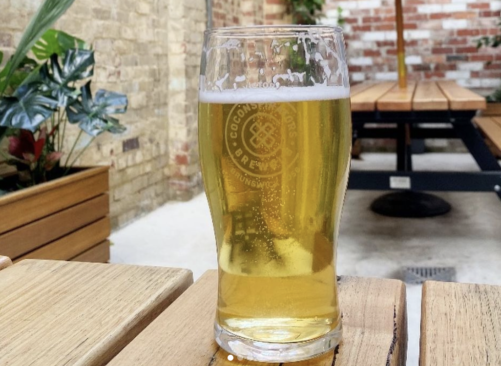 Picture of a pint of CoConspirators Brewing Company beer on a table in an outdoor beer garden