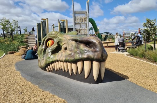 Picture of Dinosaur Park in Truganina, with a large T-Rex head poking out of the ground, and a blue sky in the background