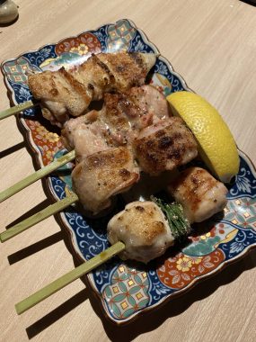 Picture of a blue and white dish with four yakitori skewers on top from Yakikami South Yarra. The dish has a lemon on the skewer