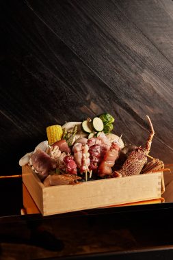 Picture of a basket of the proteins that are available for grilling at Yakikami South Yarra. The basket shows cuts of meat and vegetables and is set against a wooden wall.