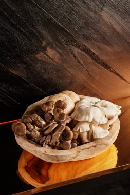 Picture of a wooden bowl with organic wild funghi inside, part of the a la carte menu at Yakikami South Yarra. The bowl of mushrooms is against a wooden wall