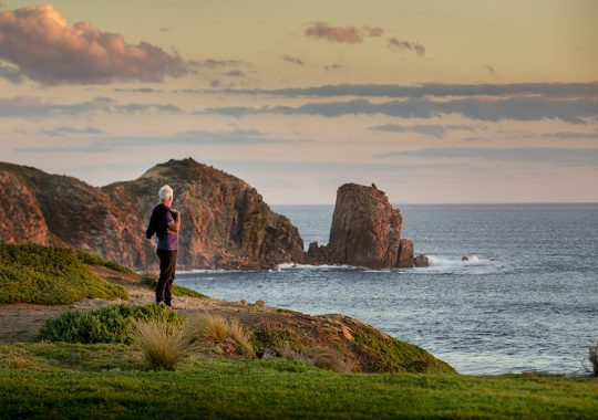 Picture of a man on trop of a cliff point in Cape Woolamai, overlooking the beach and ruggard Phillip Island landscape