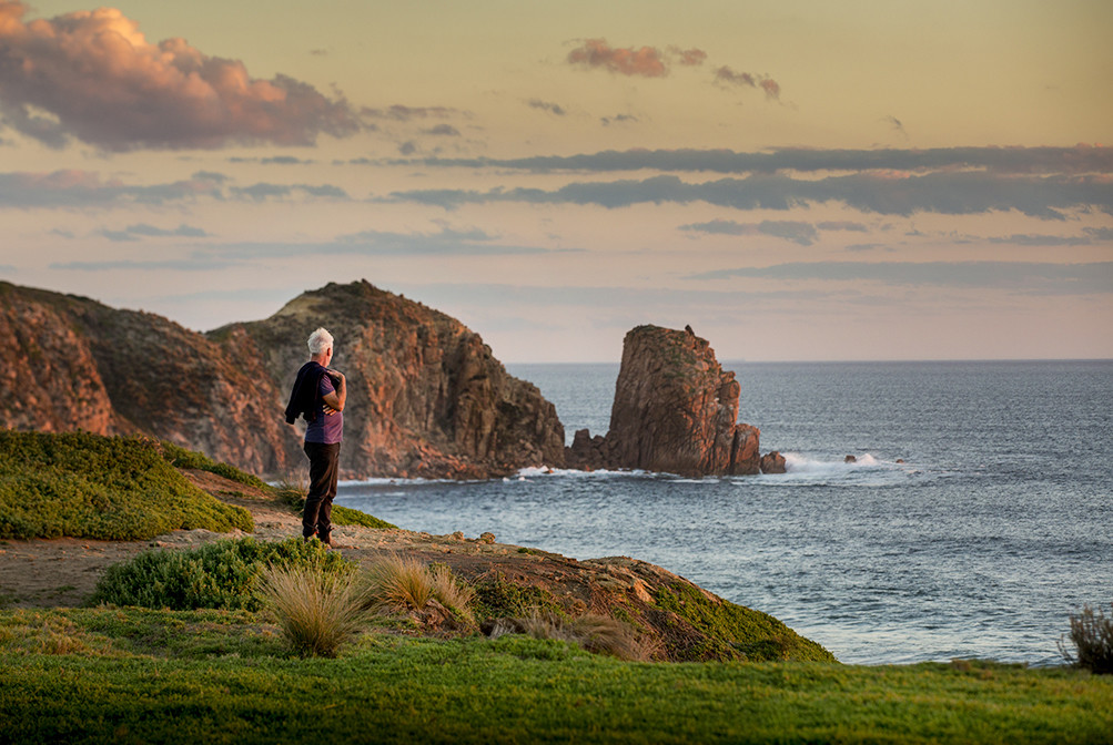 Picture of a man on trop of a cliff point in Cape Woolamai, overlooking the beach and ruggard Phillip Island landscape