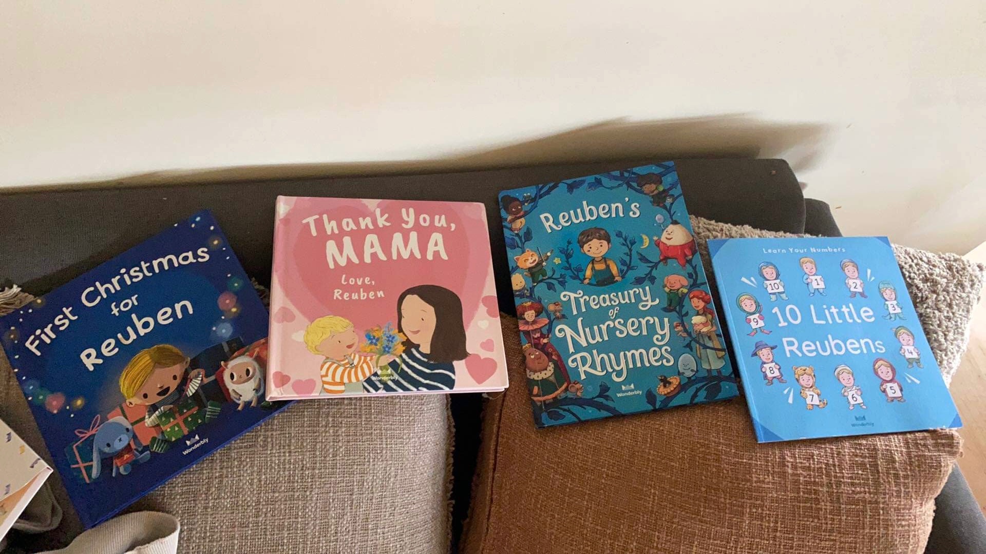 The picture of four Wonderbly books on a couch. There is a personalised Christmas book, a Mother's Day personalised book, a nursery rhyme book and a counting book from Wonderbly books