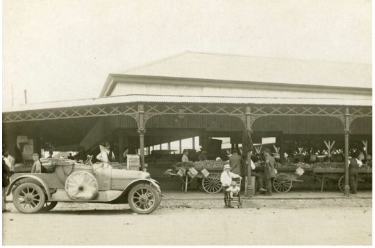 Black and white picture of South Melbourne Market in 1920, with a 1920s car parked out front and old stalls set up out-front