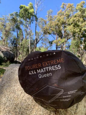 Picture of the Wanderer self inflating mattress in a bag wrapped up on a rock with a blue sky and nature in the background