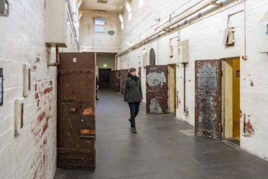 Picture of the Old Melbourne Gaol corridors, with a woman walking next to old haunted cells