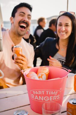 Picture of a man and a women sitting outside with a bucket of Part Time Seltzers on the table