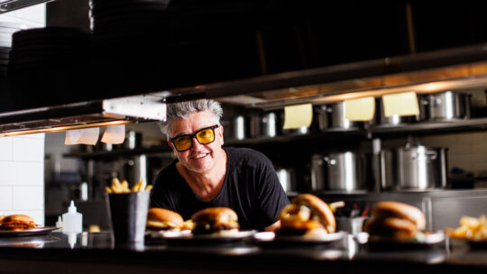 Picture of Sean Connolly in a kitchen, with Shush Burger dishes on the 'pass' ready to be served