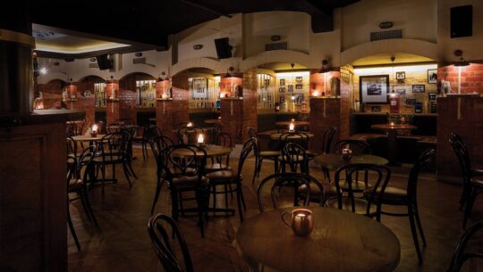 Picture of the Beneath Driver Lane bar with dim lighting and tables and chairs scattered throughout