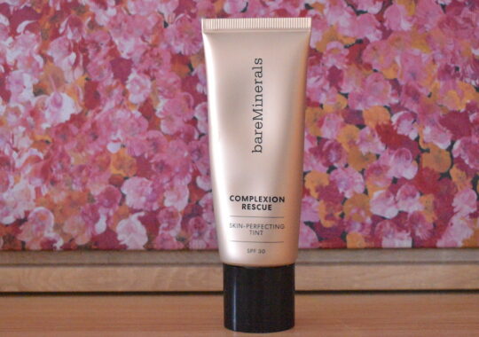 Bare Minerals Compexion Rescue bottle on a table with a pink background behind it