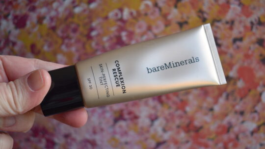 Bare Minerals Complexion Rescue tube held in front of a pink backdrop