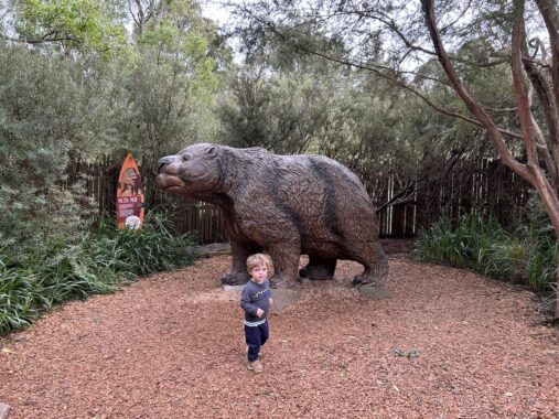 Toddler at Healesville Sanctuary playing in front of a statue of a wombat