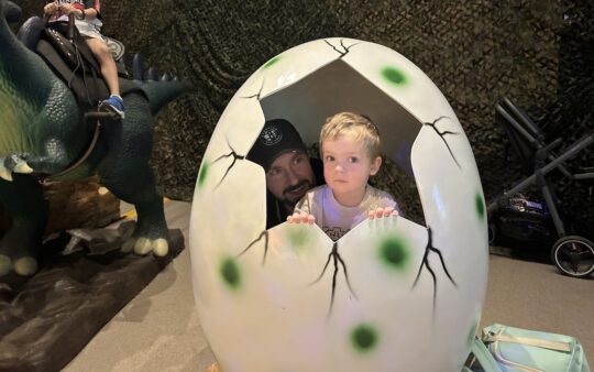 Small boy inside a dinosaur egg, poking his head out of the crack in the egg at Dinos Alive Melbourne