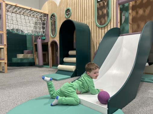 Child going down a slide at an indoor play centre in Mill Park called Eden Play. The play equipment is new and colourful and the boy is wearing all green.